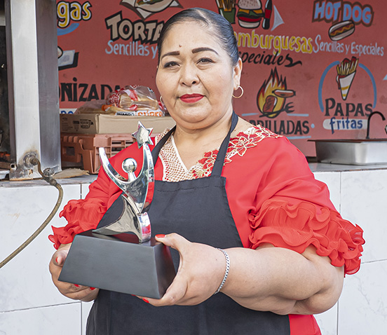 Yadira Tziu ganadora del Premio Emprendedores 2024, con trofeo en su taller de costura.
